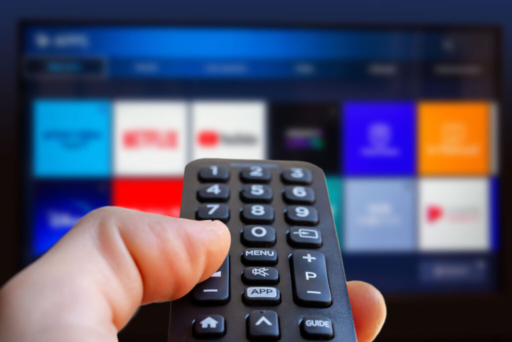 Subscription services. A man is holding a remote control of a smart TV in his hand. In the background you can see the television screen with streaming entertainment apps for video on demand.