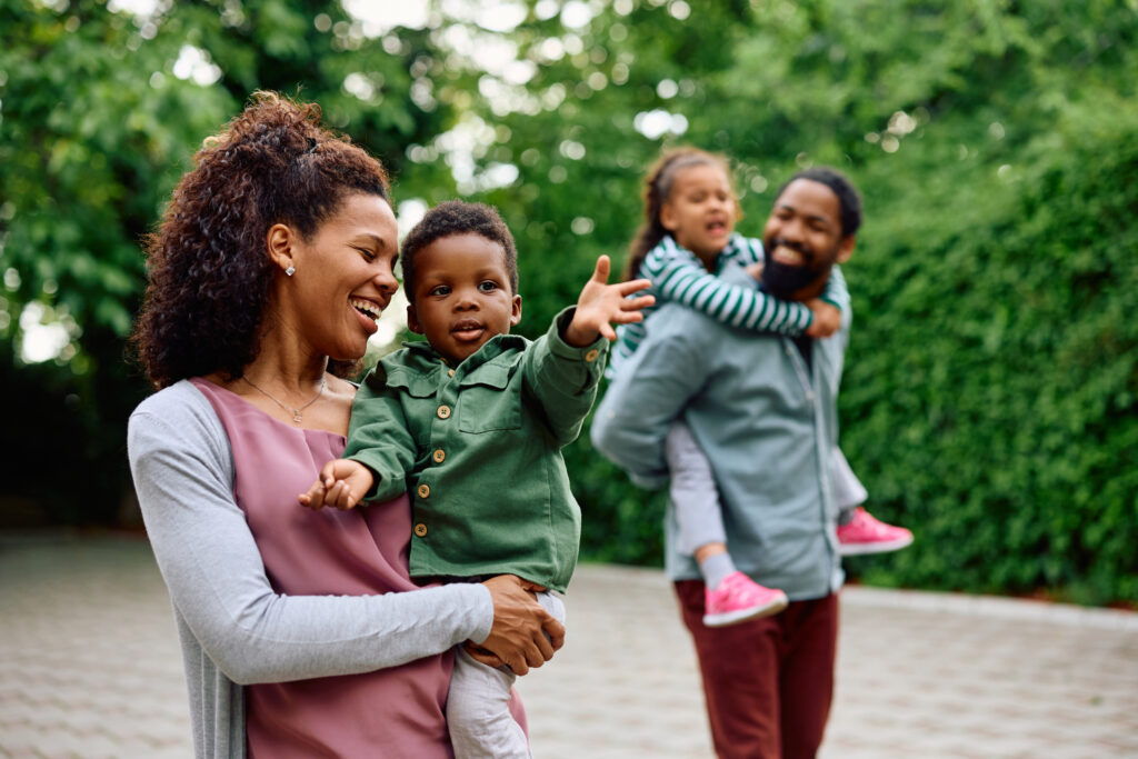 African American woman holding her small son while walking outdoors. Father and daughter are in the background.