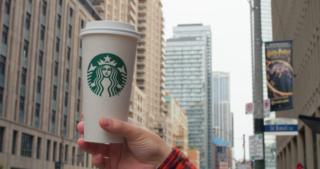 Starbucks drinks. Hand holds Starbucks cup, iconic urban backdrop. City hustle flows as Starbucks offers familiar comfort. Emblematic coffee moment in metropolitan life. Starbucks concept